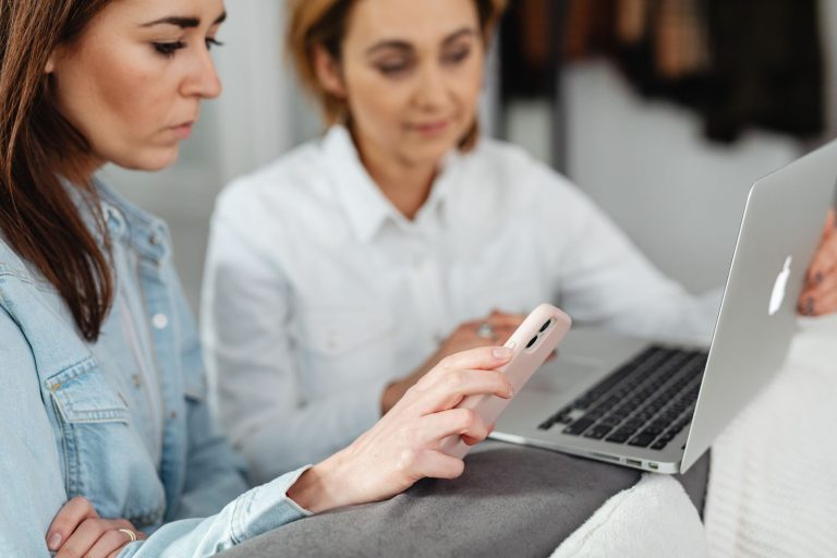 Two people looking at a smartphone together with a laptop open beside them